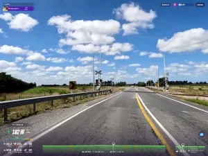 A road approaches a level rail crossing with cloudy blue skies above