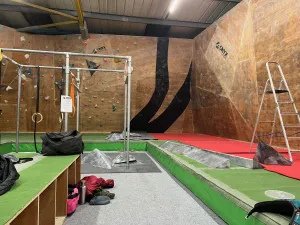 A plyboard climbing wall, half stripped of holds, half not.